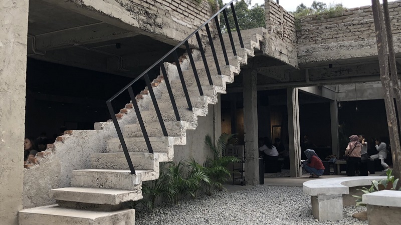 Unfinished stone building interior with concrete stairs and black metal railing, courtyard seating area