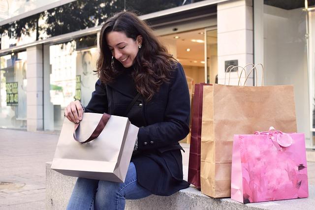 Woman smiling while shopping, carrying gift bags outside a store entrance with shopping bags and paper purchases