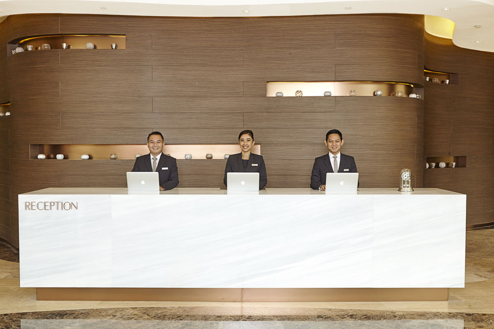 Hotel reception desk with three staff members behind it in a modern lobby with wood walls and lighting