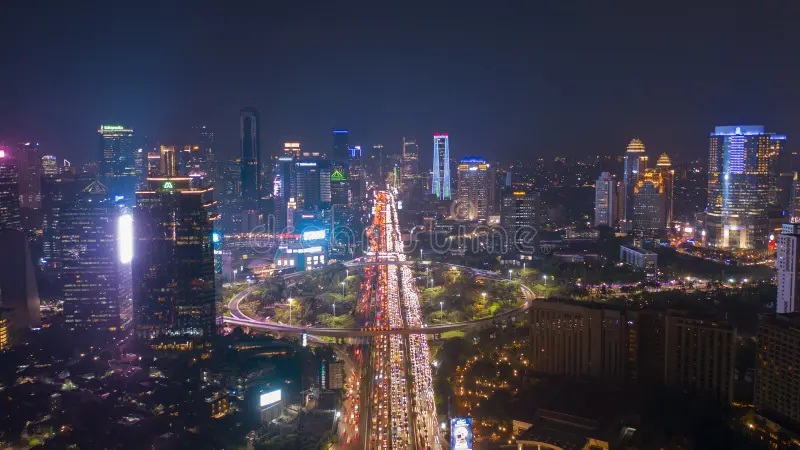 Night skyline with brightly lit city buildings and looping highways, aerial view over downtown with traffic lights