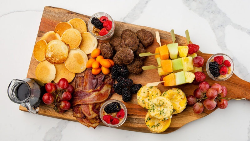 Wooden charcuterie board with meatballs, fruit skewers, brie bites, grapes, berries, and crackers