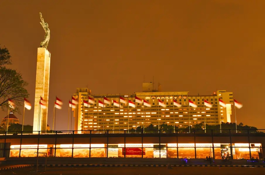 Illuminated Indian building at dusk with tall monument statue and warm city skyline lights