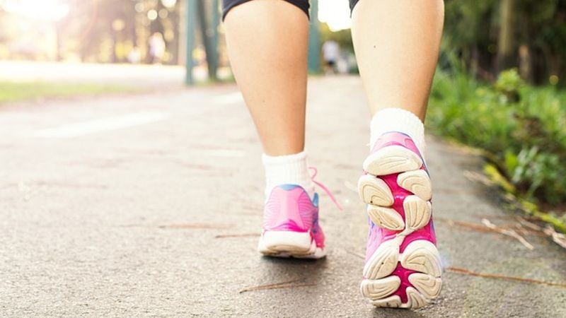 Running shoes and legs walking along a sunny outdoor path with soft bokeh background