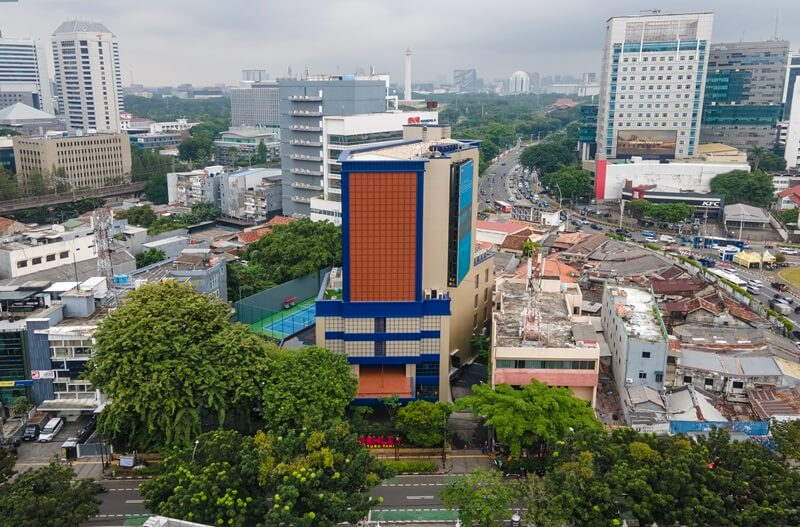 Aerial view of a city skyline with tall office buildings, roads, and an orange-and-blue tower in Jakarta Indonesia