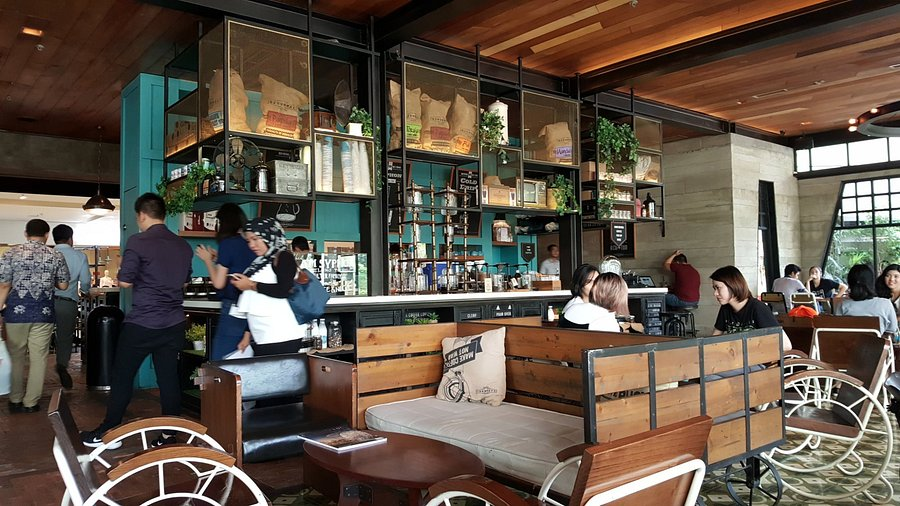 People dining and bar staff serving drinks at a modern cafe with wooden benches, shelves, and hanging lights