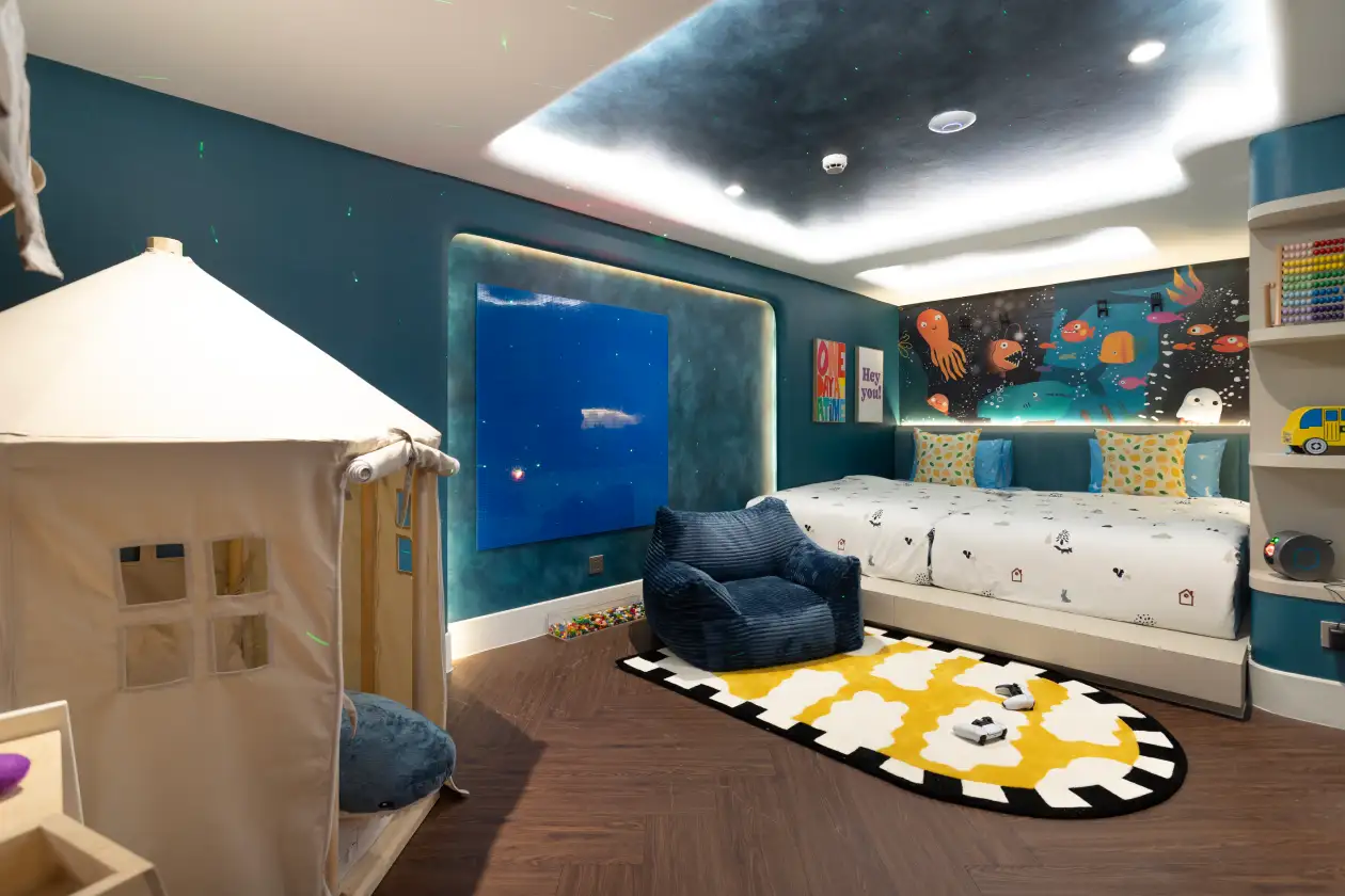 Kid’s playroom with blue ocean-themed wall mural, window panels, bean chair, bed with cartoon bedding, and play tent