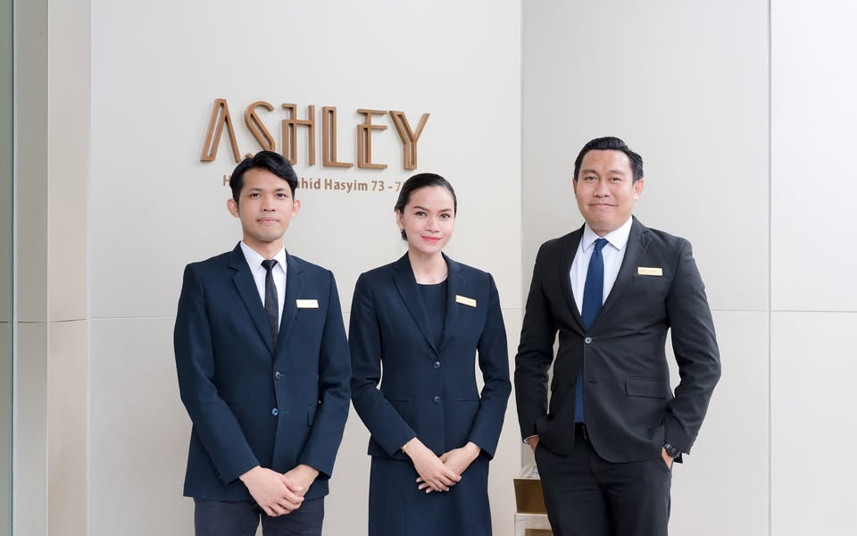 Professional hotel staff in navy suits standing in front of the Lobby signwall with “A S H I L T Y” lettering