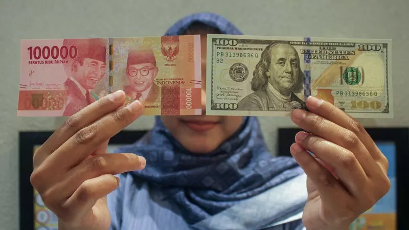 Hands holding Indonesian rupiah and US $100 bills in front of a person in a blue scarf