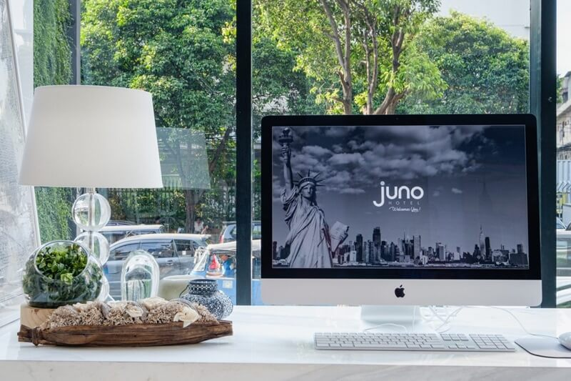 Juno hotel website displayed on an iMac monitor on a desk beside a white lamp and decorative tray