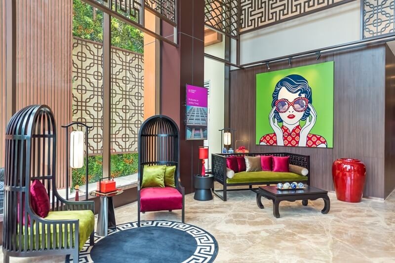 Modern hotel lounge with green art portrait wall painting, colorful chairs, sofa, and red decor vases