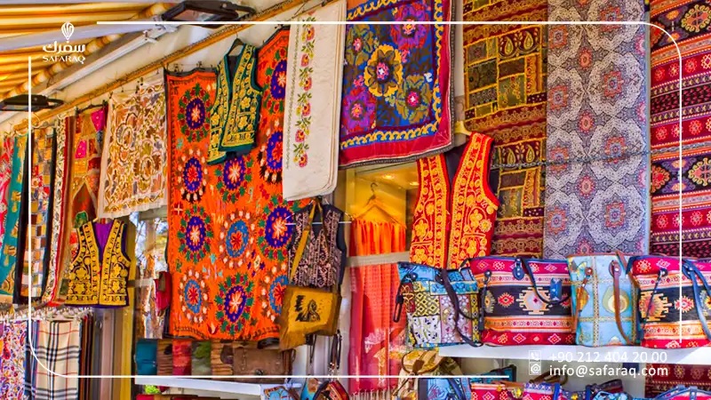 Colorful patterned Persian rugs hanging in a market stall, with scarves and textiles for sale