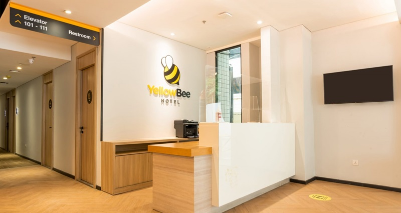 YellowBee Hotel reception desk in modern lobby with hallway signs for elevator and restroom