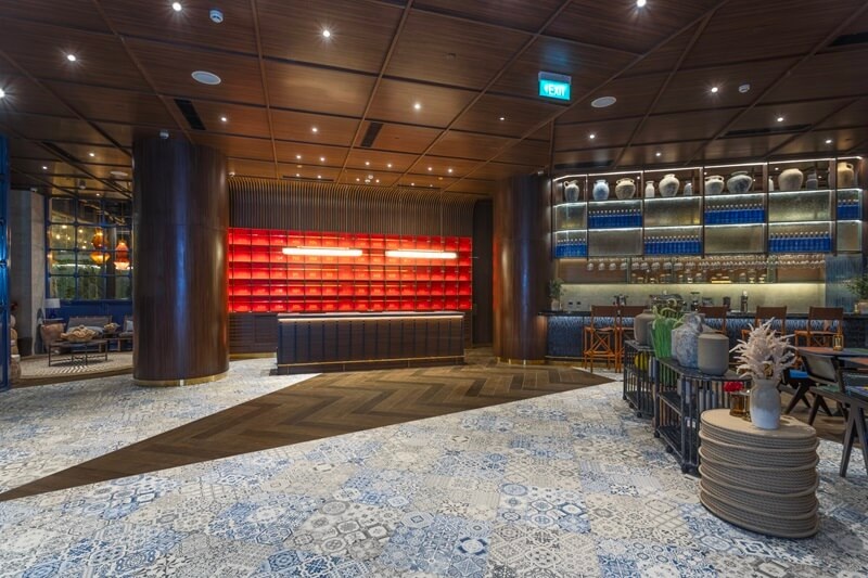 Modern hotel lounge interior with patterned tile floor, bar shelving with blue lighting, and seating area
