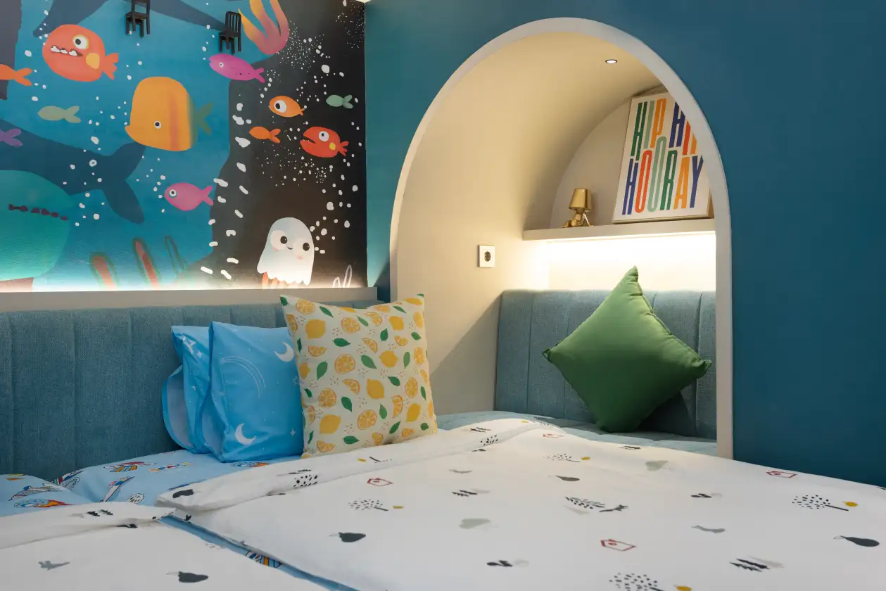 Kid’s bedroom with blue sea-themed mural, arched window alcove, and neatly made bed with colorful pillows