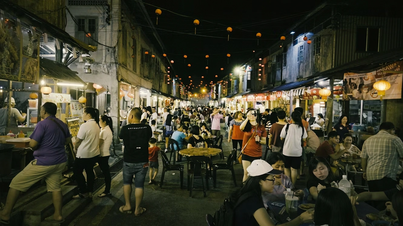 crowded night market street with people eating at outdoor tables
