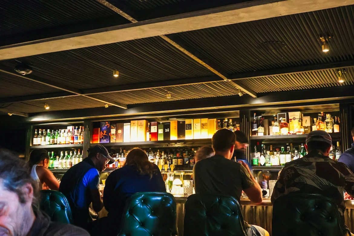 dimly lit bar counter with patrons seated on stools