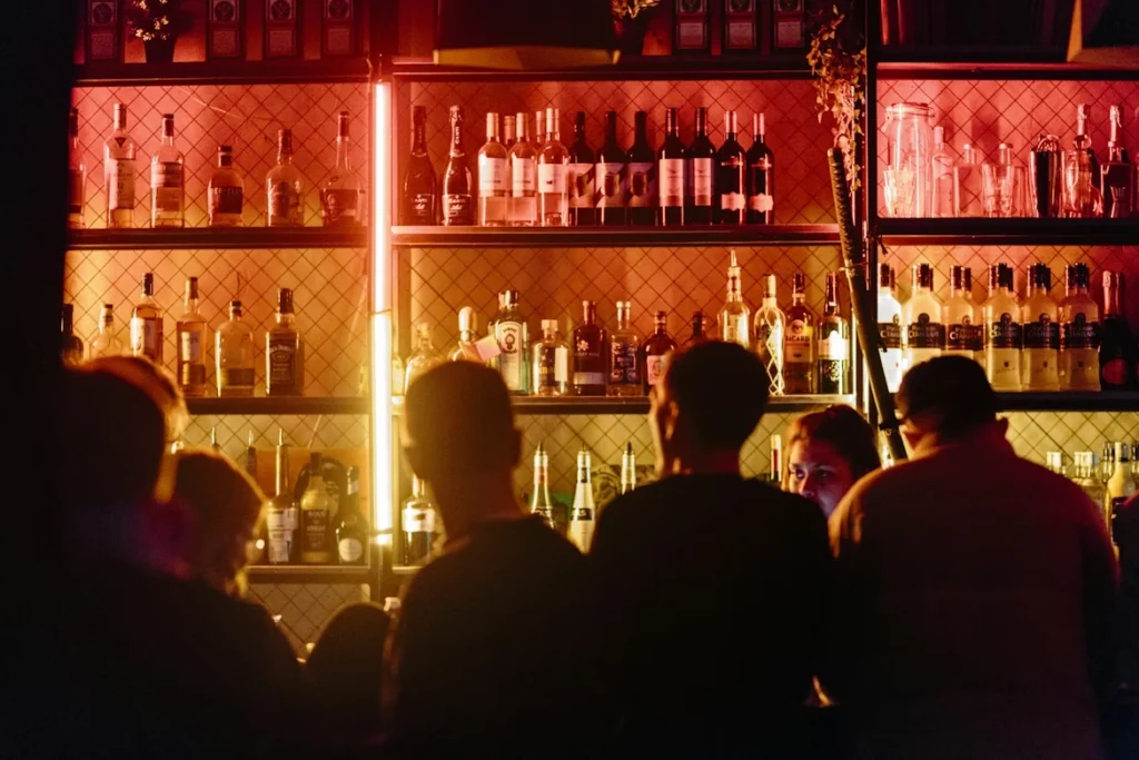 dimly lit cocktail bar with patrons seated at back-lit liquor shelf counter
