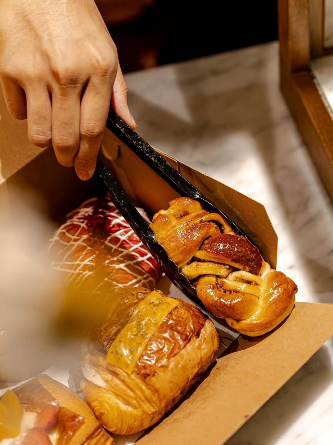 hand placing a fresh pastry into a takeaway box with tongs