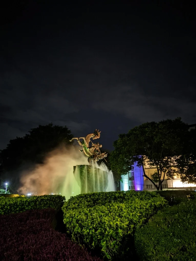 illuminated statue fountain surrounded by lush greenery at night