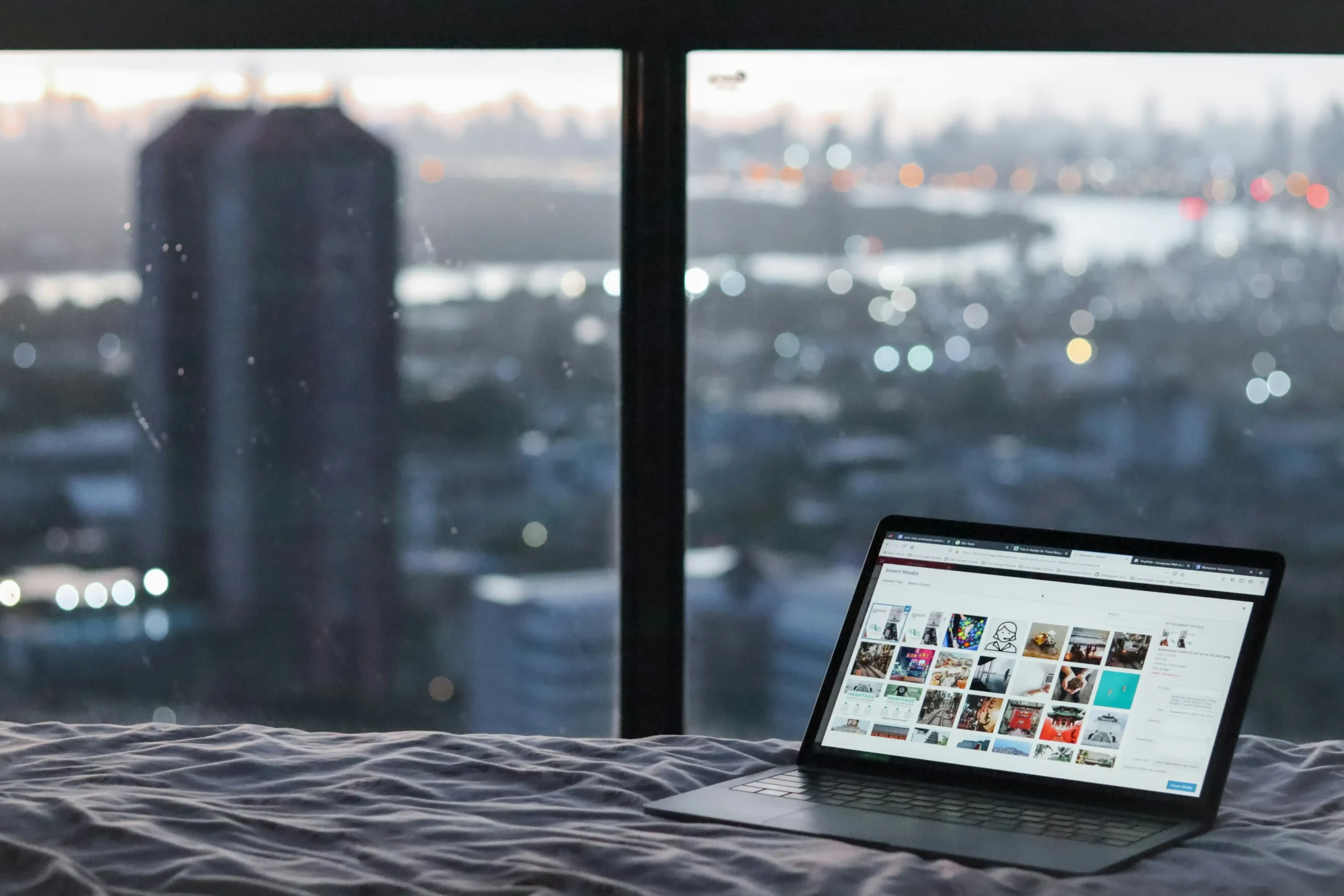 laptop on bed with city lights background