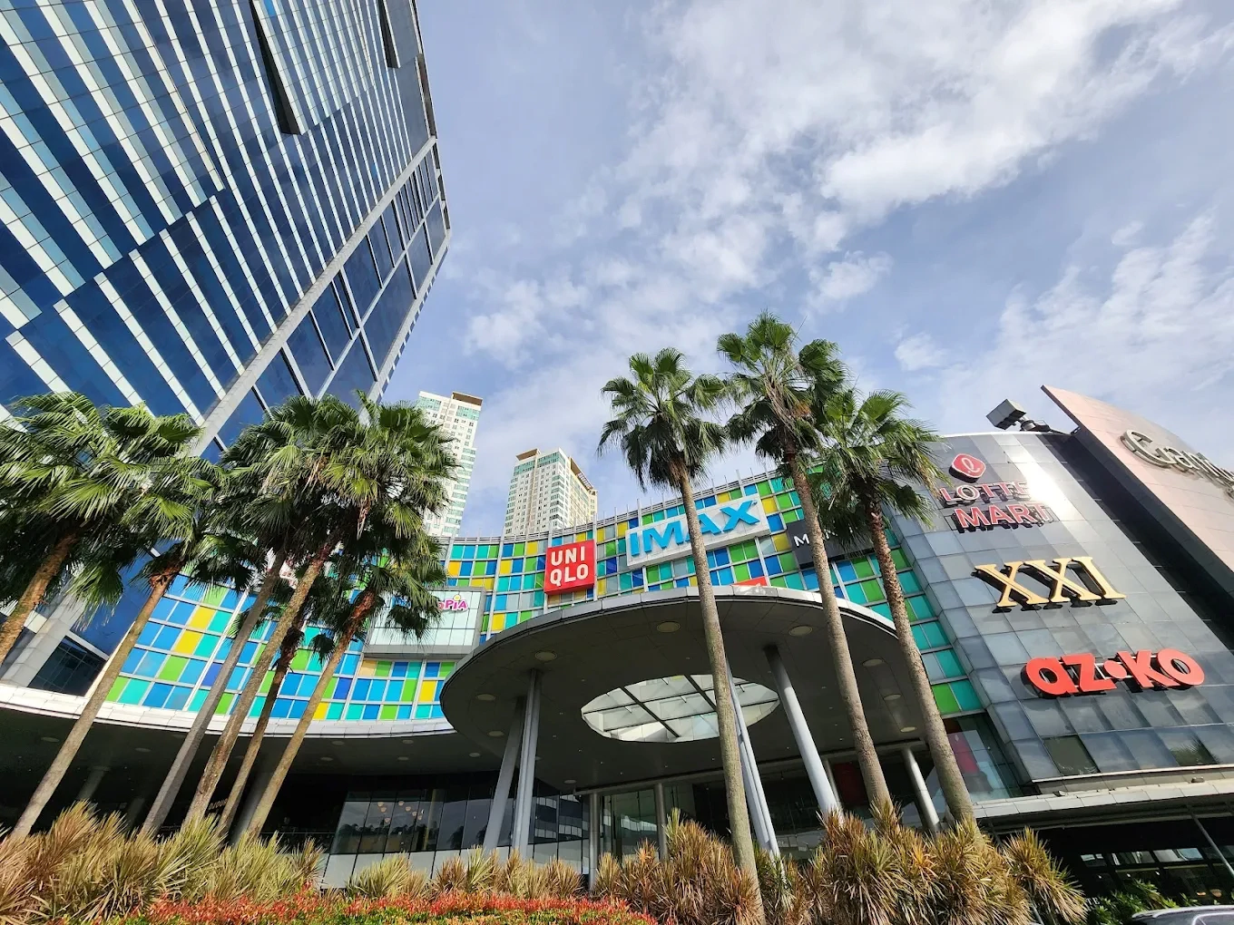 low-angle view of gandaria city mall facade with store logos and palm trees