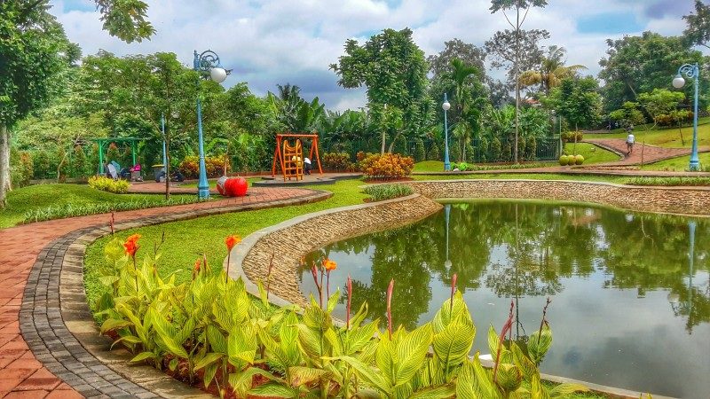 lush green park with a scenic pond brick path and yellow flowers