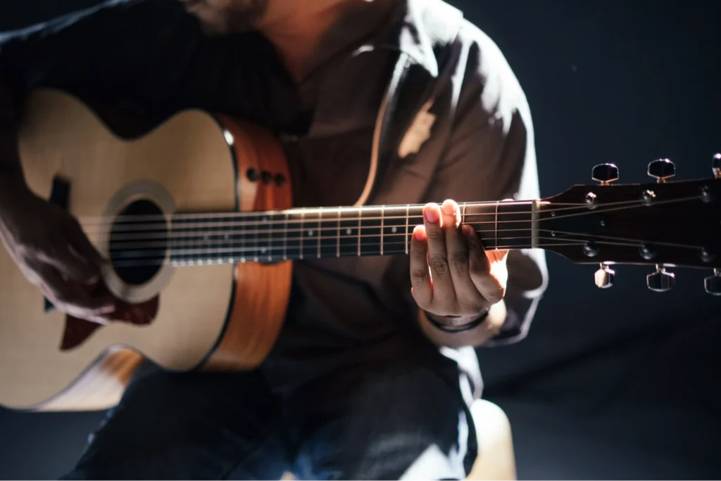 musician playing acoustic guitar under spotlight
