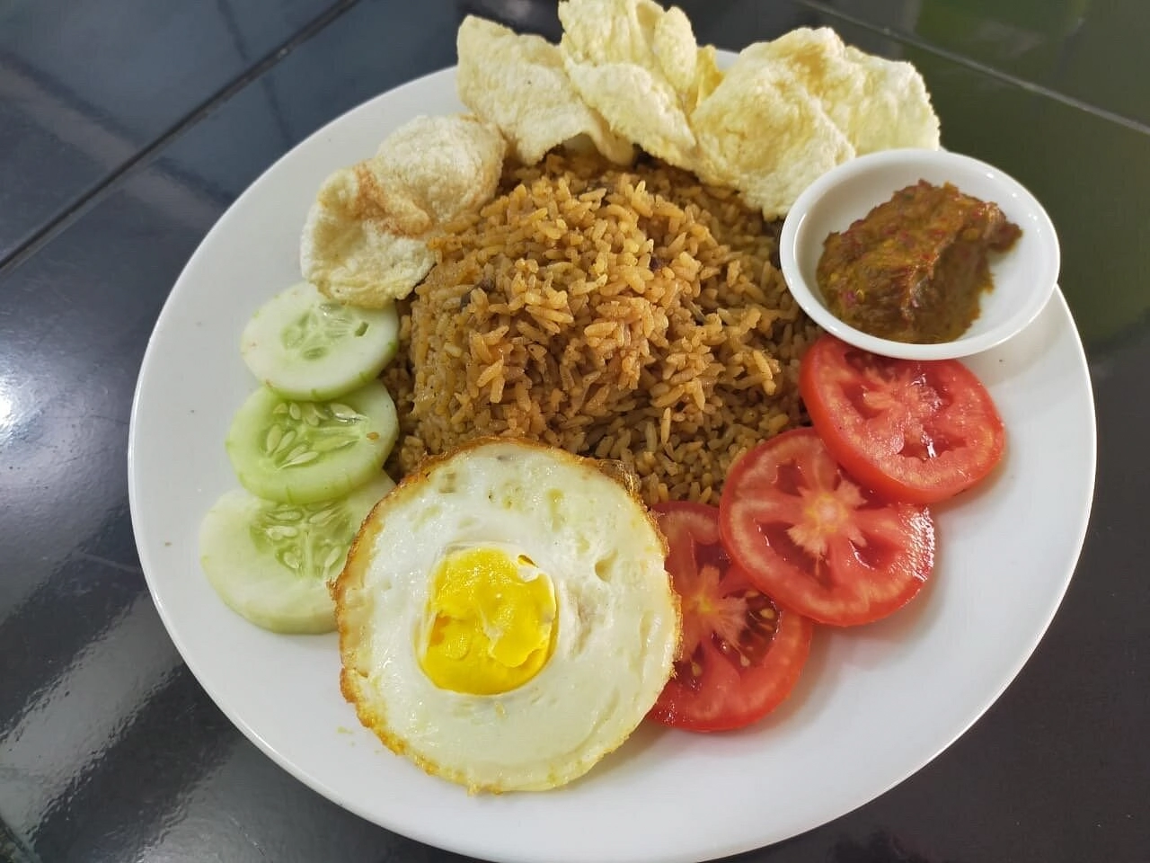nasi goreng served with fried egg sliced cucumbers and tomatoes