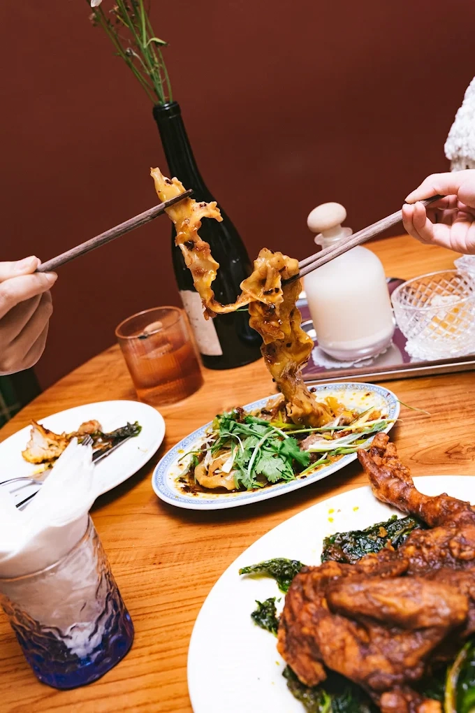person picking up a wide noodle with chopsticks from a plate on a wooden table
