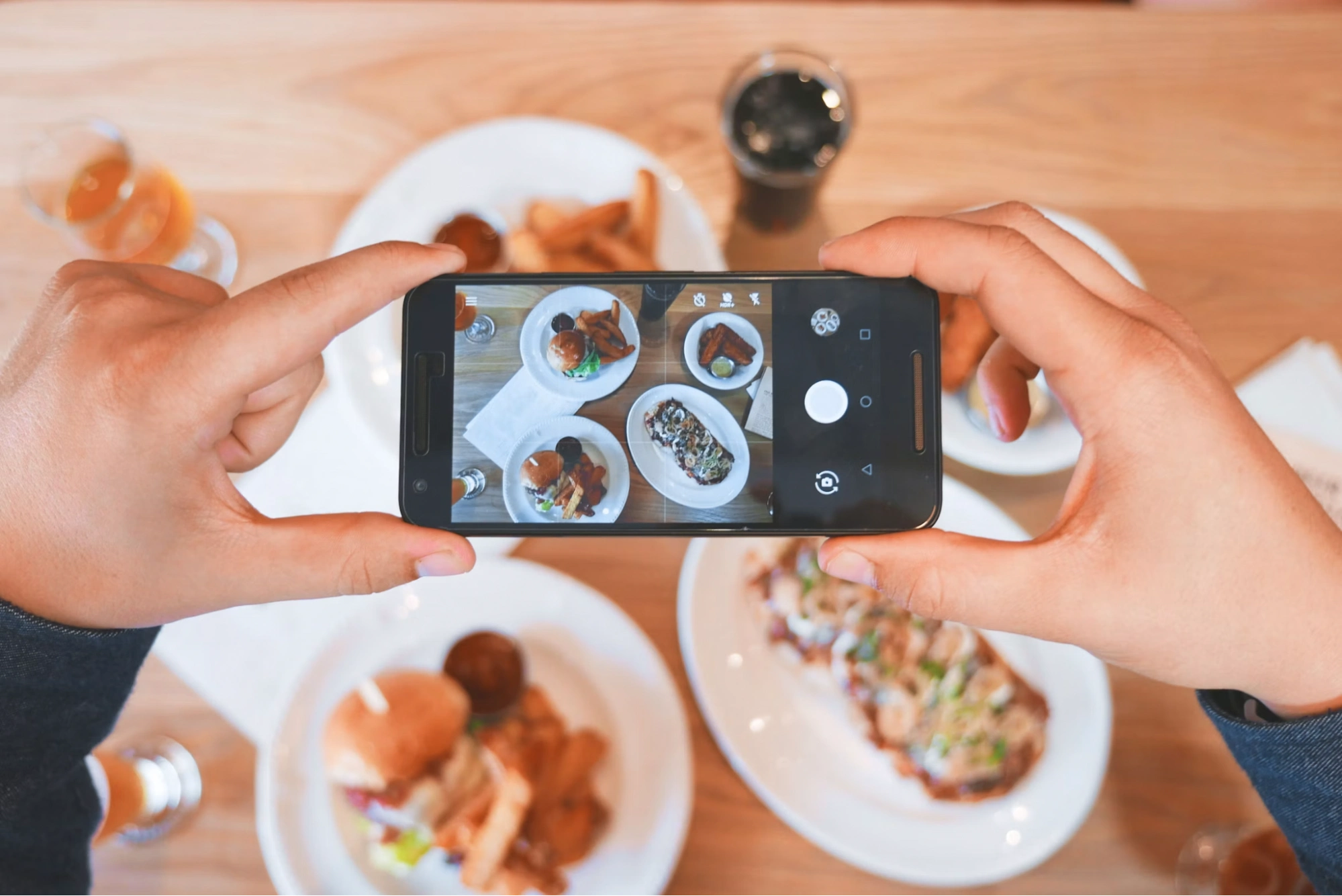 person taking a overhead photo of burgers and fries using a smartphone
