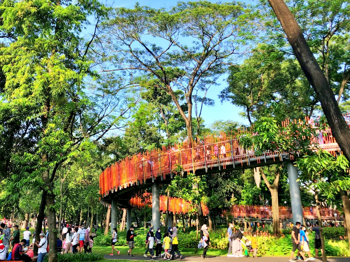 raised walking bridge with orange railing and people in a park