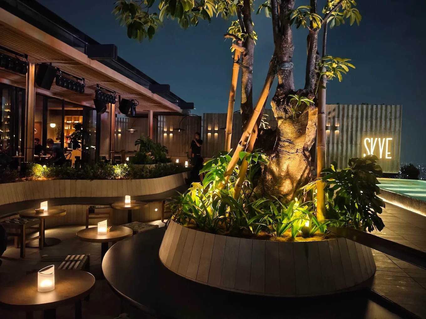 skye rooftop lounge with lit tables and lush plants at night