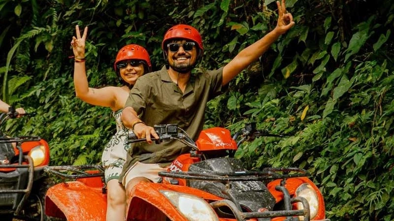 smiling couple riding an orange atv through lush green foliage
