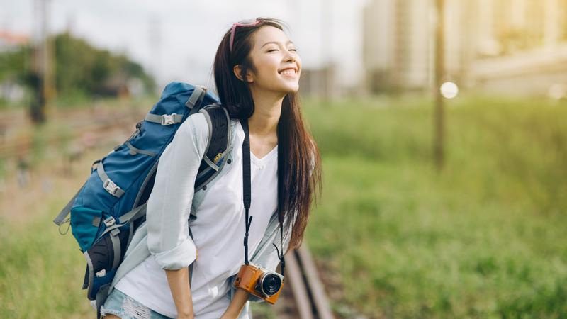 smiling female backpacker with a camera standing near train tracks