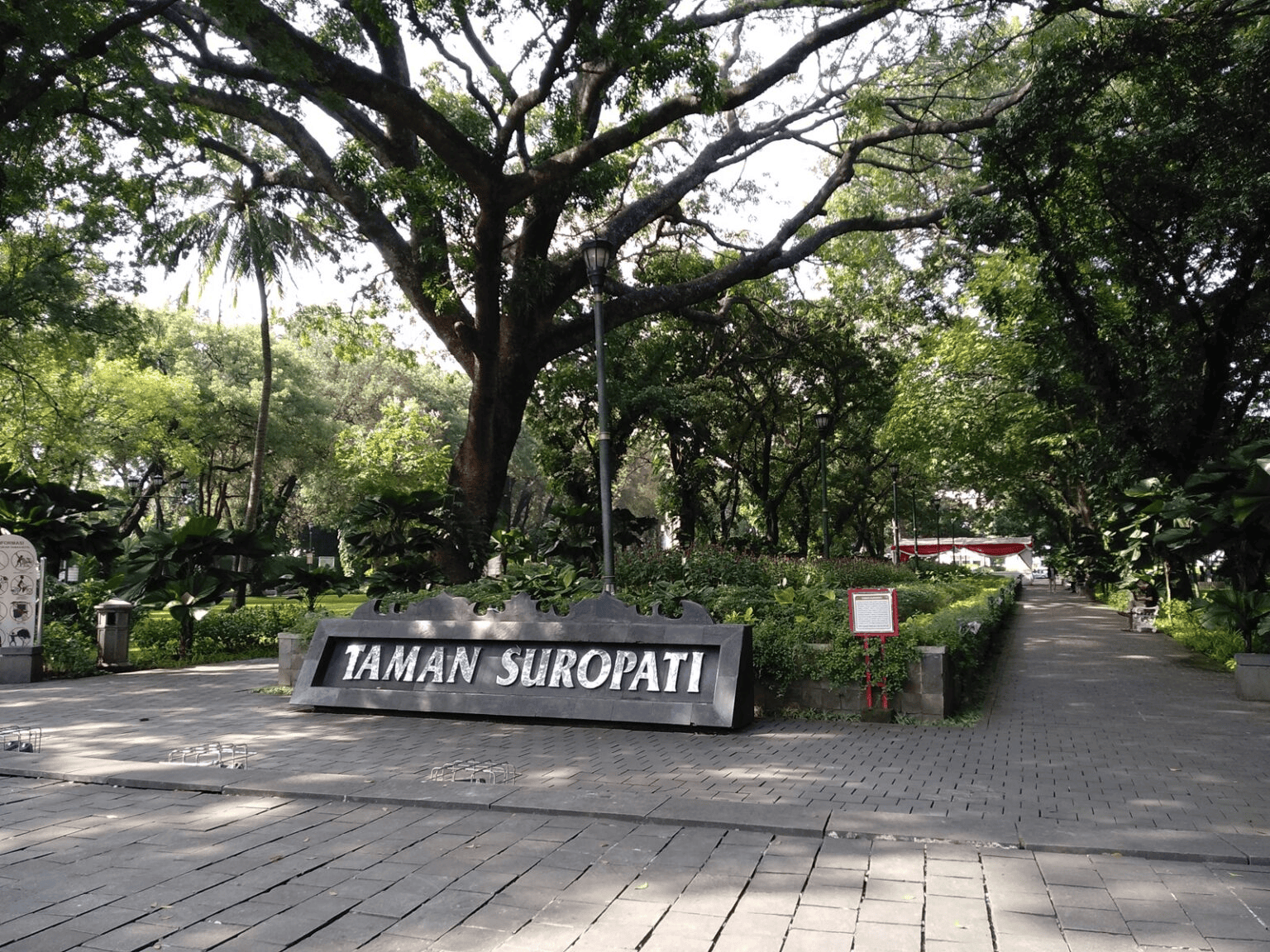 taman suropati park sign under large shade trees with stone path