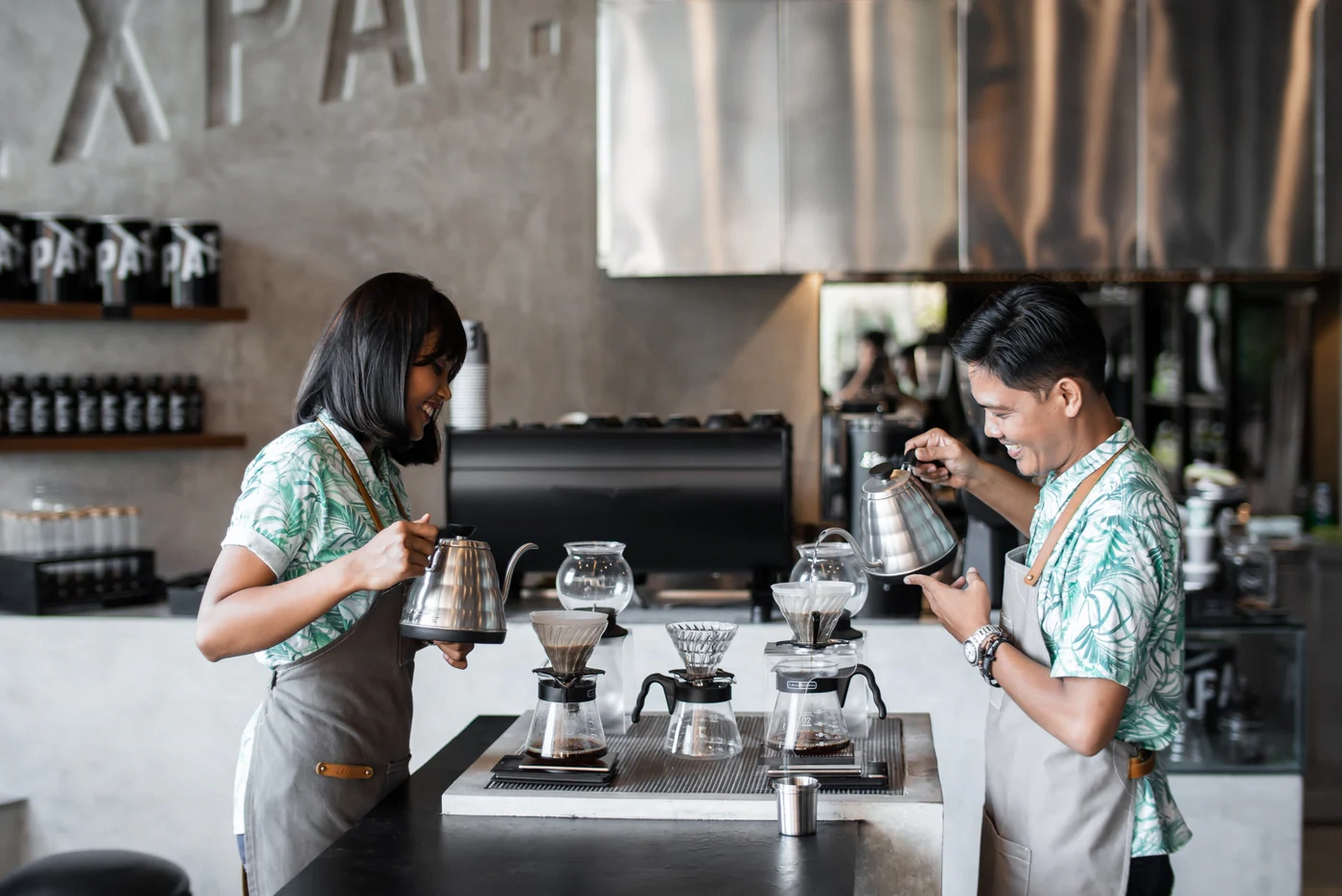 two baristas pouring coffee using pour-over equipment in a cafe