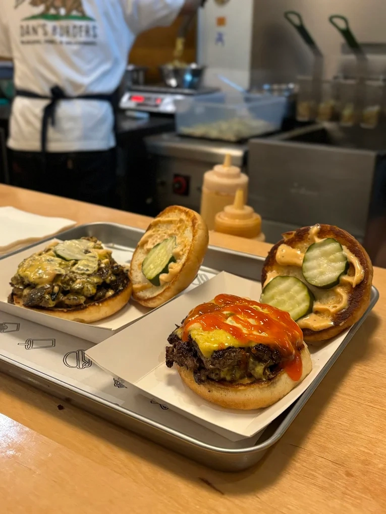 two gourmet smash burgers with melted cheese and pickles on a metal tray
