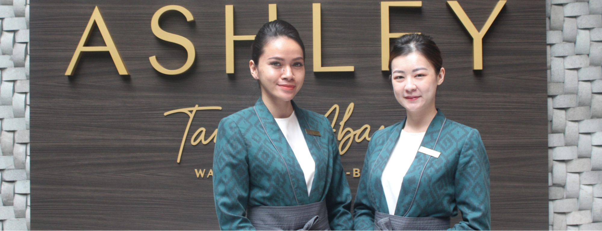 two smiling female hotel staff members in matching teal uniforms
