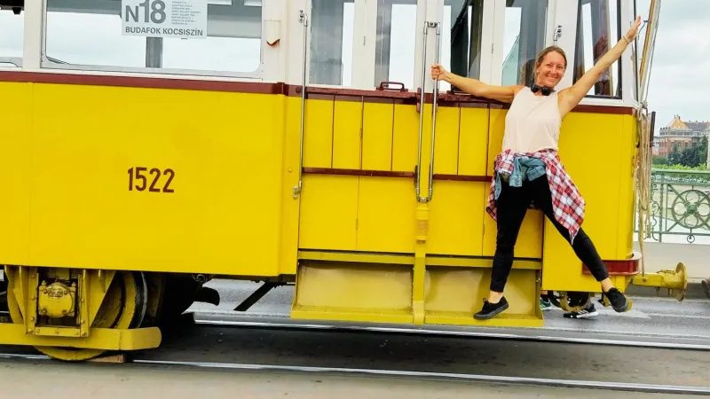 woman posing happily on the steps of a yellow city tram